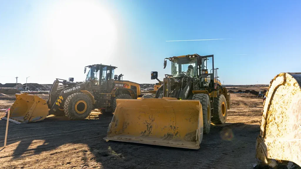 Two of ReadyDig's XCMG wheel loaders at a jobsite, including a ReadyDig-branded loader, positioned for heavy-duty earthmoving tasks in bright daylight.